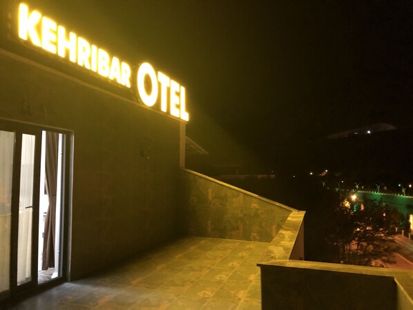 The exterior of the Khehibar Hotel with a prominent illuminated sign, a modern entrance, and a view of the surrounding area at night.