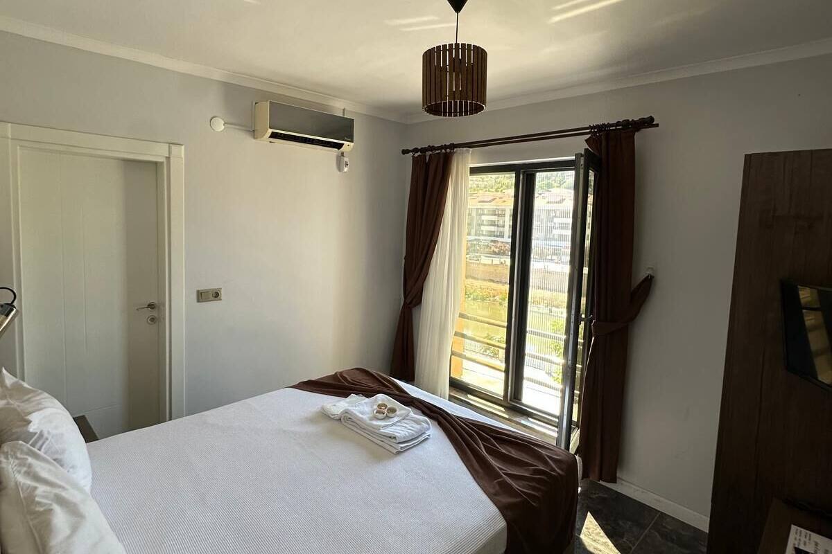 Une chambre d’hôtel avec un lit, une fenêtre avec des rideaux, un luminaire au plafond et une armoire.
