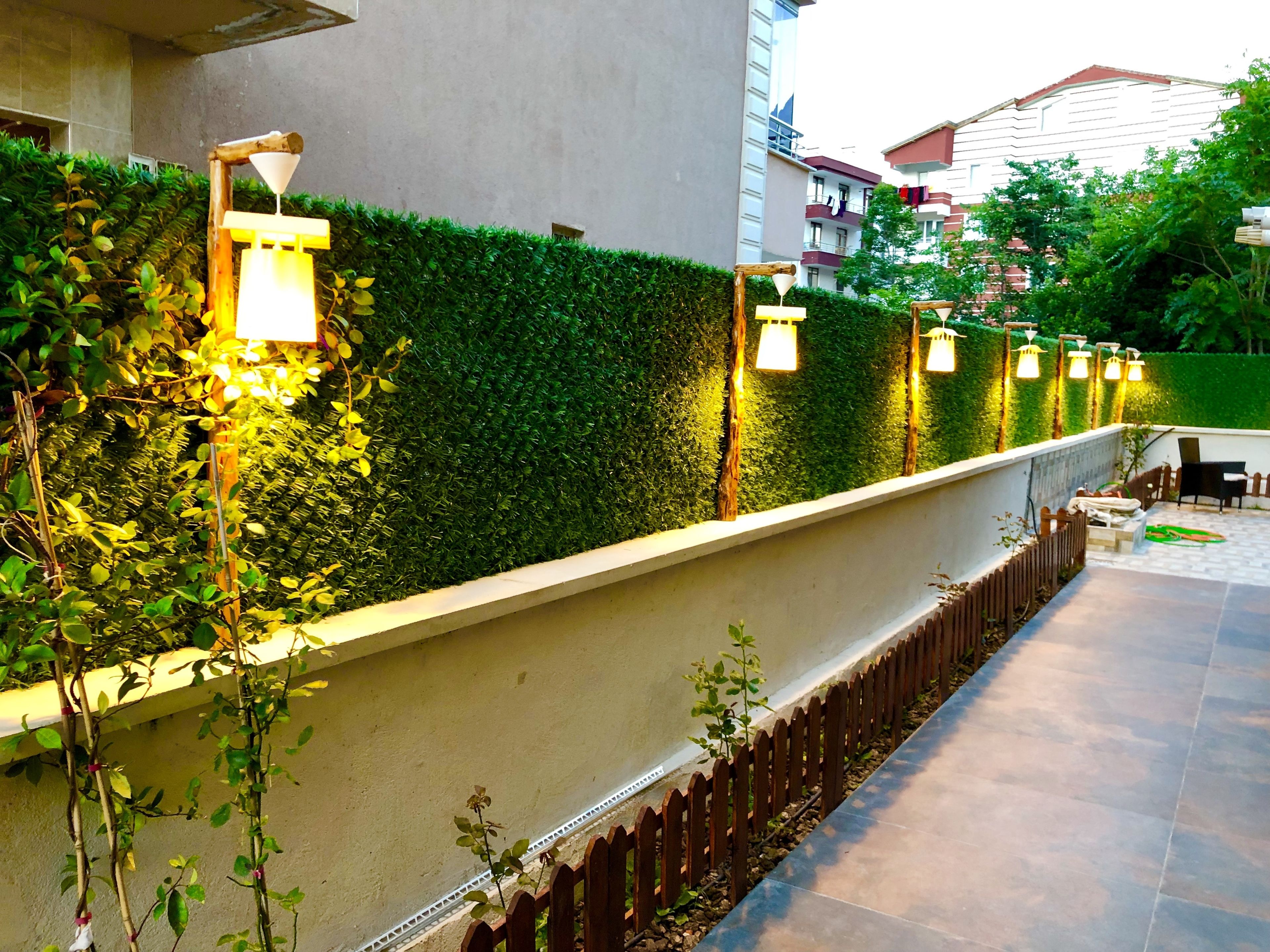 Un área exterior ajardinada con un muro bajo, una cerca de madera y un camino pavimentado.