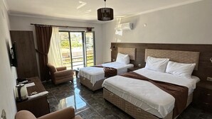Een hotelkamer met een groot bed, twee kleinere bedden, een slaapbank, een bureau en uitzicht op het omliggende landschap.