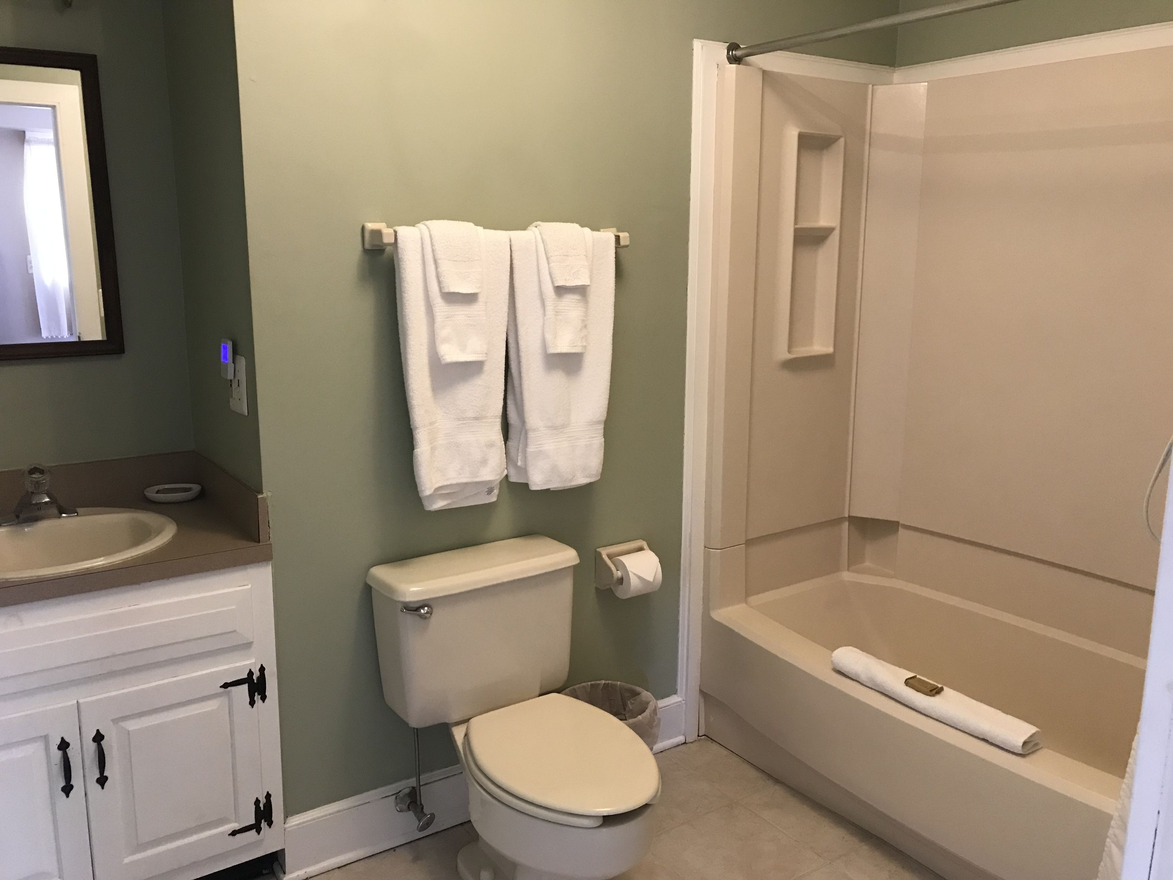 A bathroom with a toilet, sink, and shower. There are towels hanging on the wall.