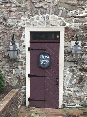 A stone building with a dark brown door, a sign reading "The Inn at Millrace Pond," and two lantern-style lights on either side of the door. - Inn at Millrace Pond (Blairstown)