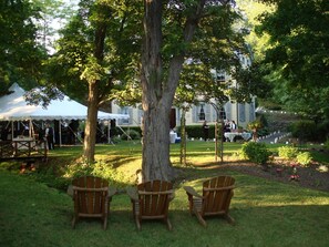 Un jardin avec trois chaises en bois, un grand arbre et, au fond, une tente blanche.