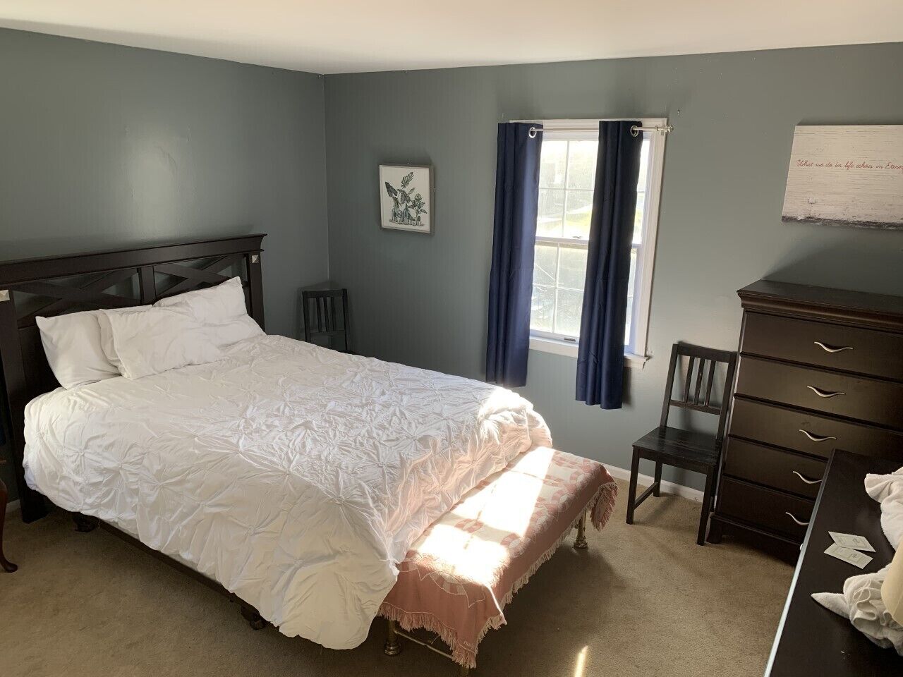 Une chambre avec un grand lit, une commode, une chaise et une fenêtre avec des rideaux.