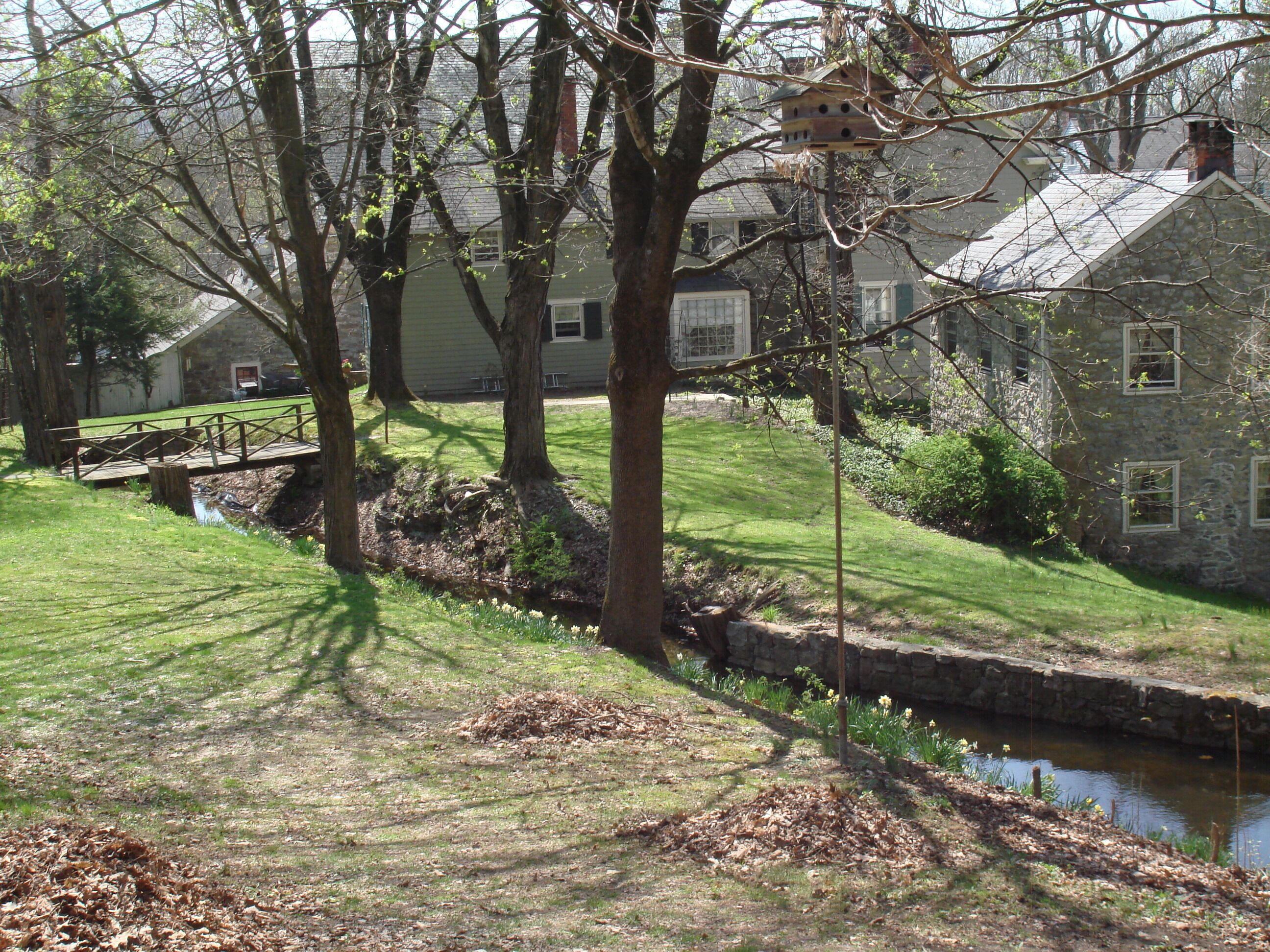A stone house with a small stream and a wooden bridge.