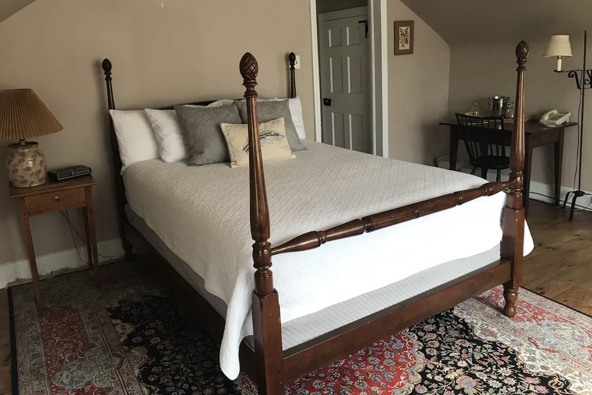 Un dormitorio con cama con dosel, una mesita de noche con lámpara, una silla y un escritorio con lámpara.