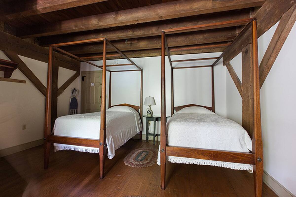 Una cama con dosel de madera y ropa de cama blanca en una habitación con vigas de madera en el techo.