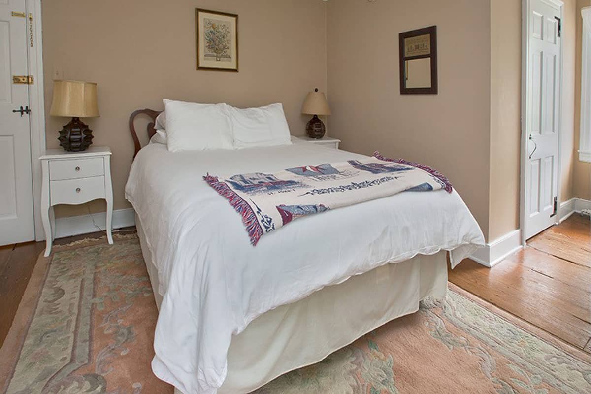 Un dormitorio con una cama grande, dos mesitas de noche con lámparas, una alfombra estampada y una puerta.