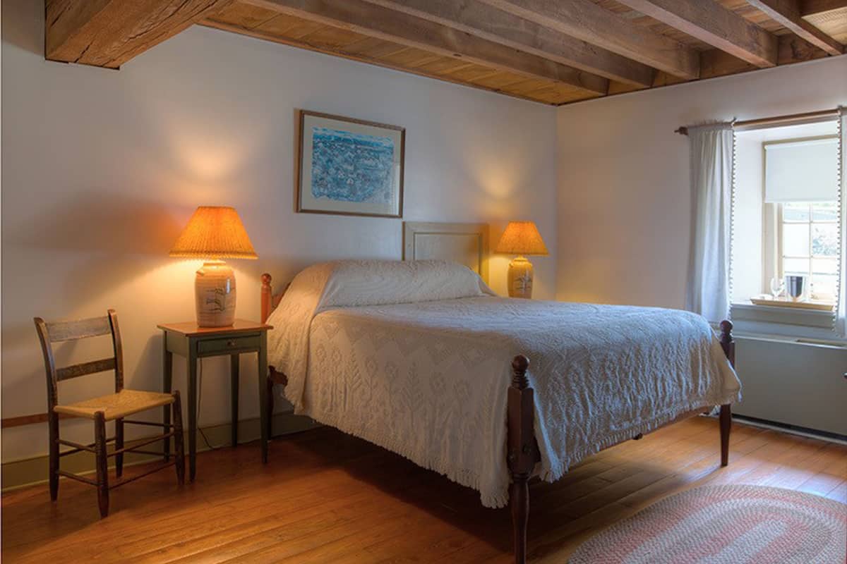 Un dormitorio con una cama de madera, dos lámparas de noche, una silla y una ventana con cortinas.