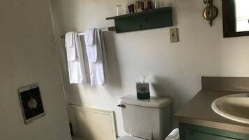 A bathroom with a toilet, a sink, a towel rack with towels, a tissue box, and a shelf with toiletries.