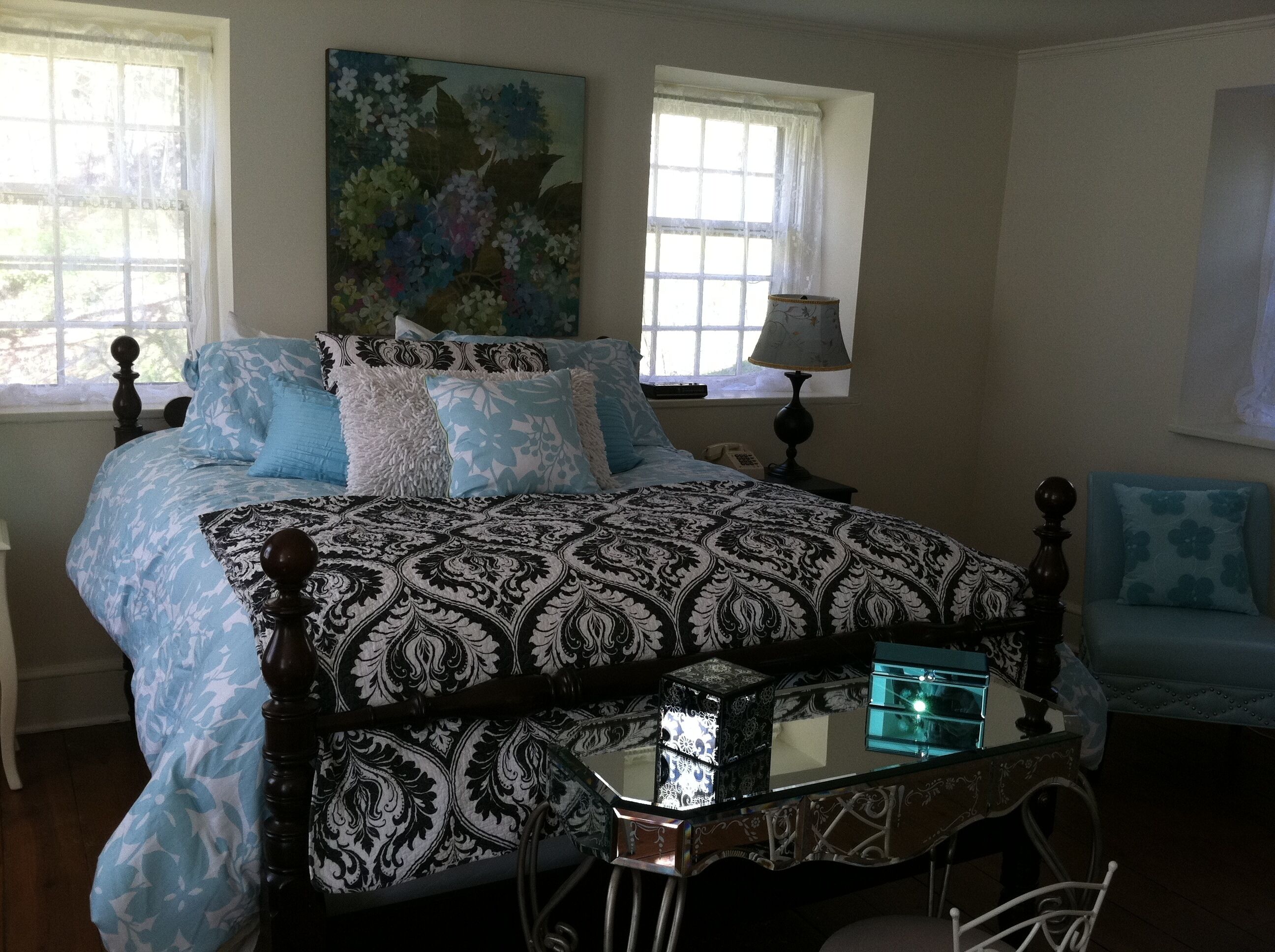 A bedroom with a large bed, a bedside table with a lamp, a chair, and a painting on the wall.