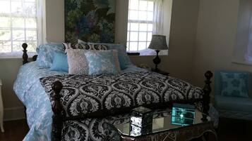 A bedroom with a large bed, a bedside table with a lamp, a chair, and a painting on the wall.
