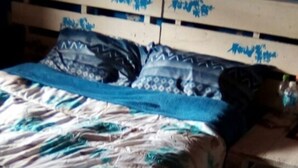 Ein Bett mit floraler Tagesdecke und blau-weißen Kissen.