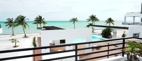 Uma varanda com vista para uma praia, palmeiras e uma piscina.