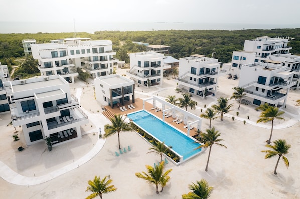 Surrounded by palm trees and lush greenery, this resort features a central pool and white buildings with balconies.