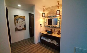 A hallway with a wooden floor, a painting of a Buddha, a sink with a bowl, and a mirror with a decorative frame.