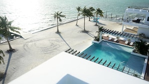 Relax by the serene pool surrounded by palm trees and lounge chairs, with ocean views.