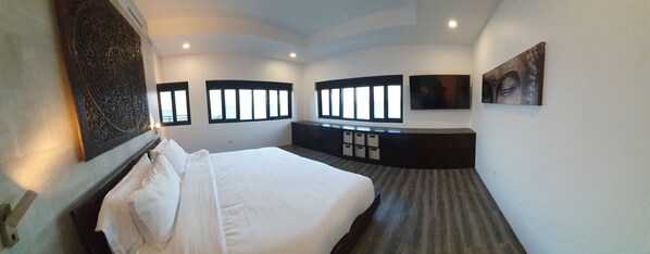Ein modernes Hotelzimmer mit einem großen Bett, integrierten Stauraumlösungen, einem Flachbildfernseher und großen Fenstern.