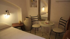Une chambre à coucher comprenant un lit, une table de chevet, un grand vase, deux chaises, une petite table avec une théière, une étagère avec des livres et un miroir.