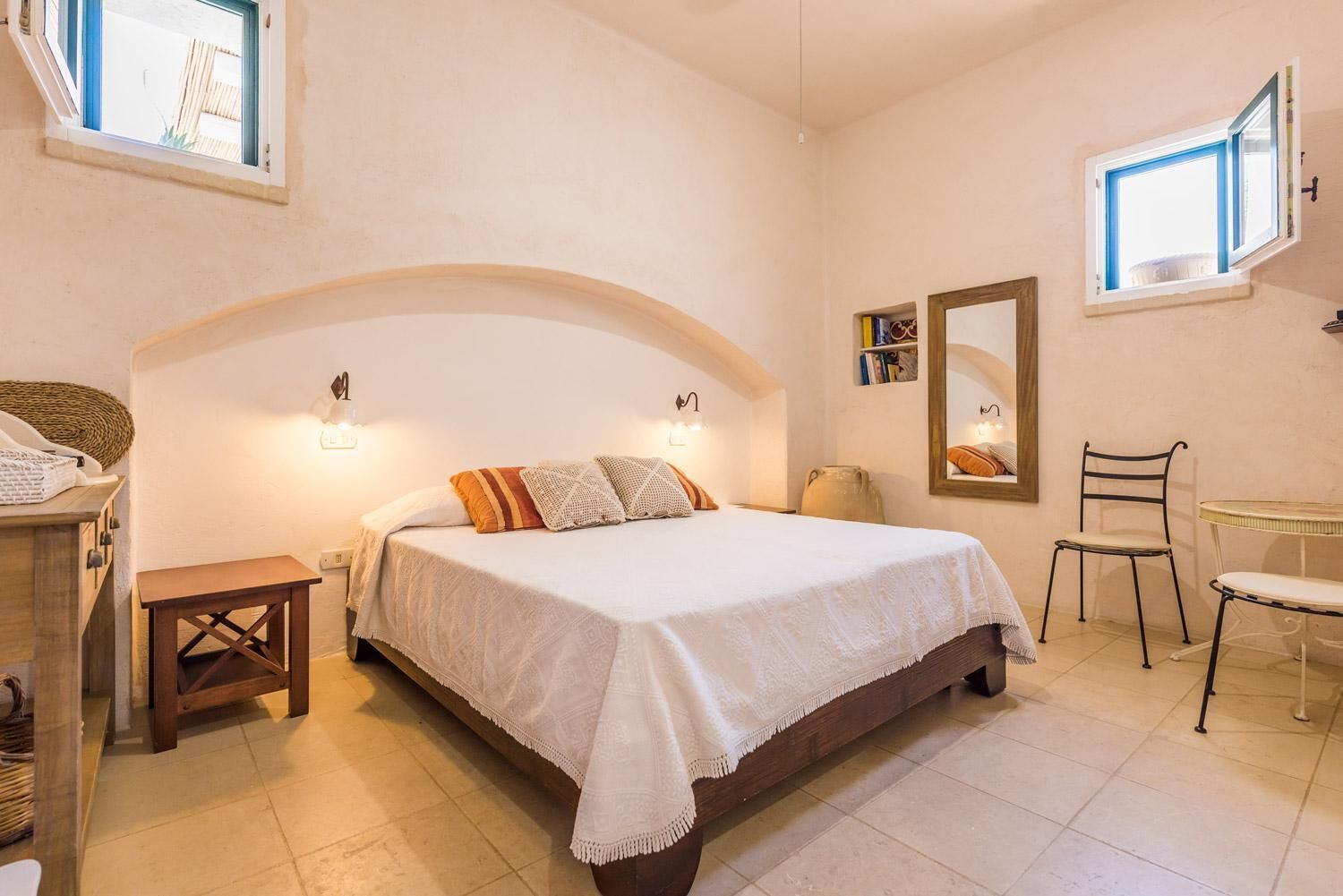A bedroom with a bed, bedside table, chair, and a small table with a lamp.