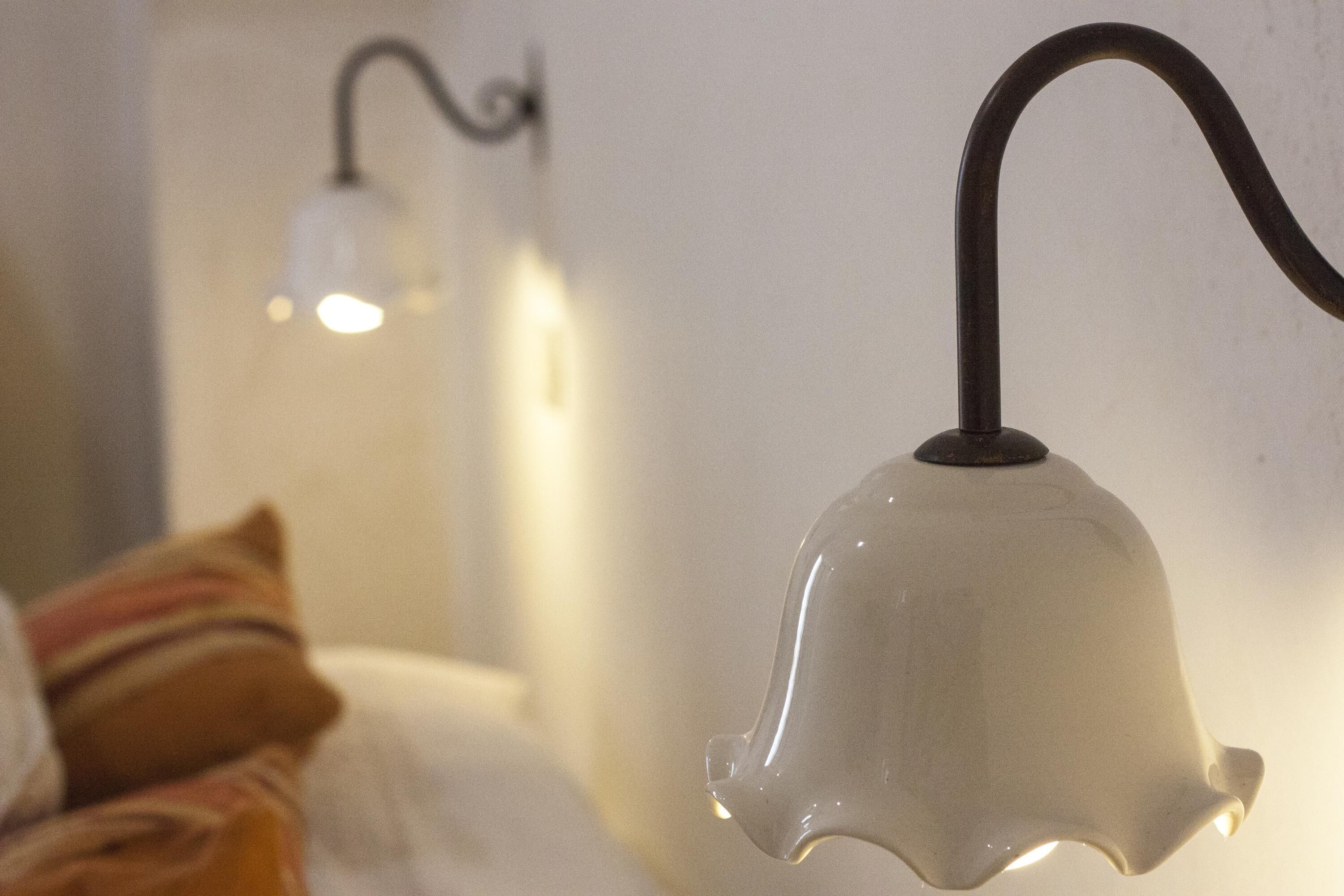 Gros plan d’un luminaire suspendu blanc, en forme de cloche, doté d’un bras incurvé et fixé au plafond.
