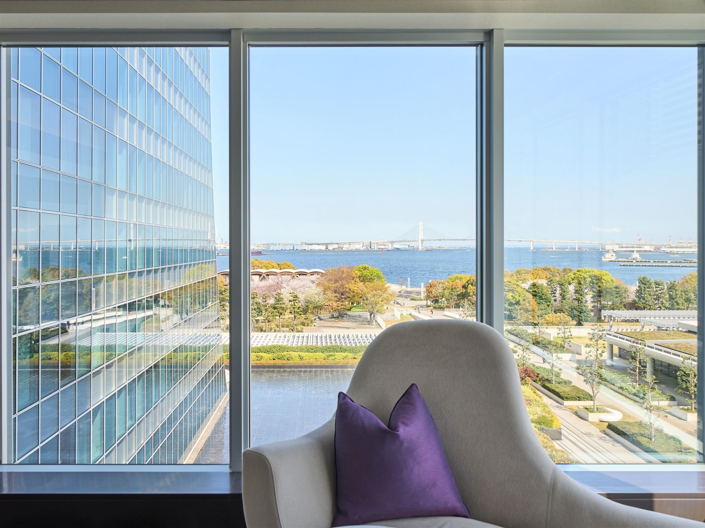 A modern office chair with a purple cushion, positioned in front of a large window overlooking a cityscape with a bridge and river.