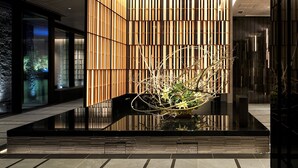 A modern lobby with a reflective water feature, wooden slats, and a glass partition.