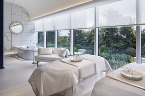 A modern spa room with a large window, a bathtub, and a massage table.