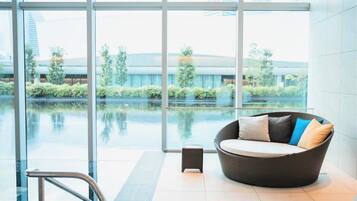 A modern indoor space with large windows, a wicker sofa with cushions, and a small table.