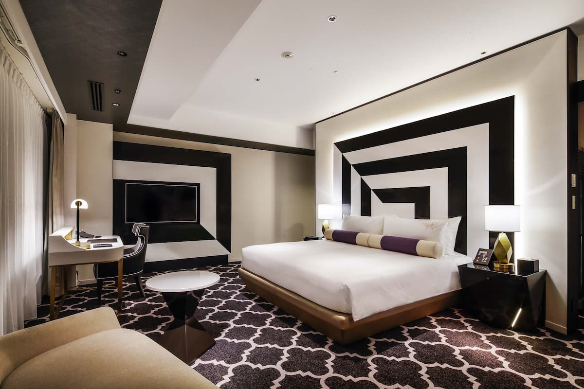 Ein Hotelzimmer mit einem großen Bett, einem Schreibtisch mit Stuhl, einem Fernseher und einem kleinen runden Tisch.