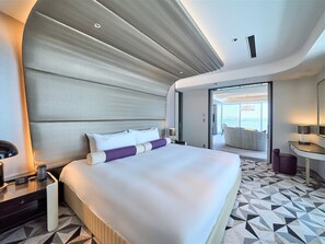 A modern hotel room with a large bed, a bedside table, a desk, and a view of the outside.