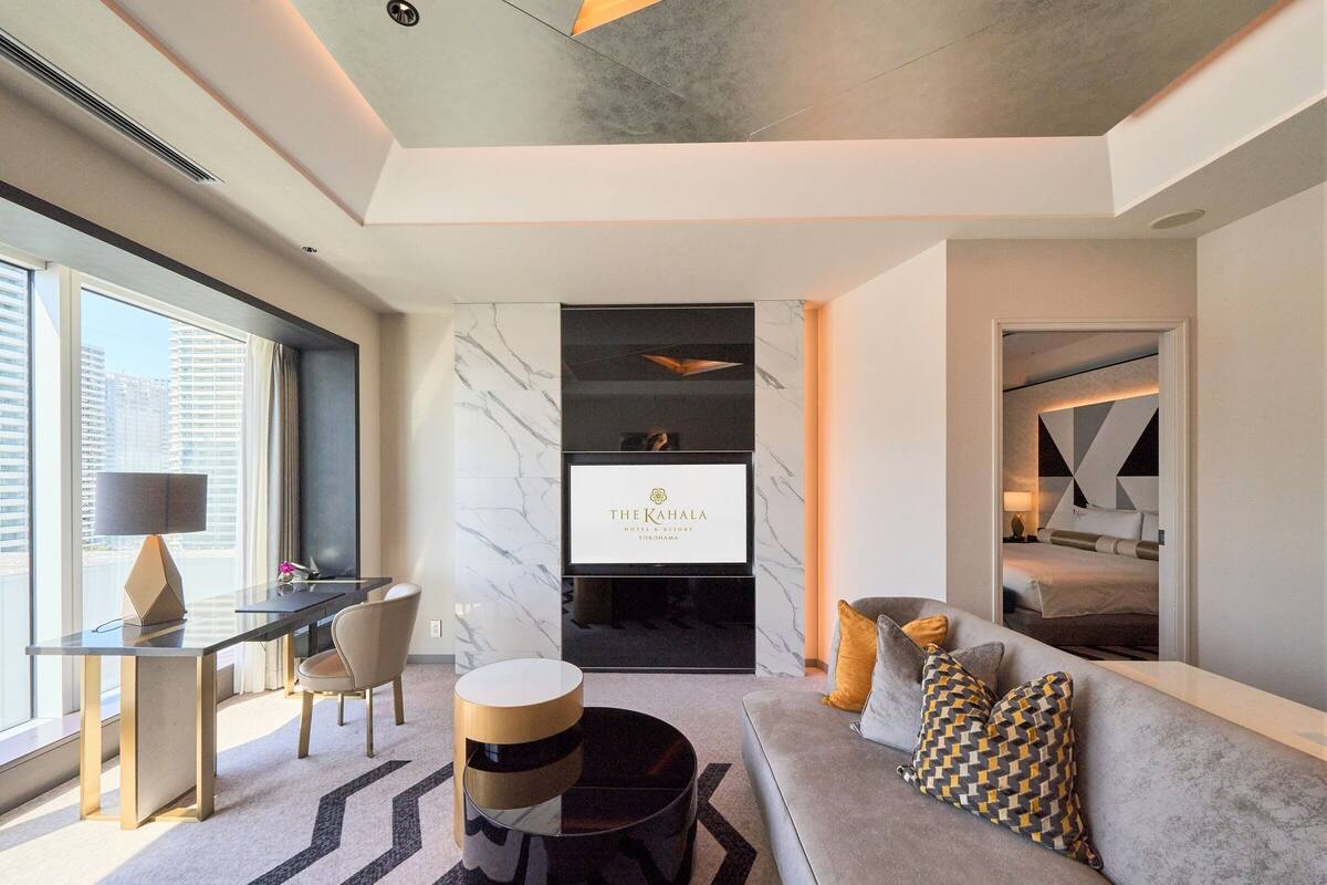 Ein modernes Hotelzimmer mit Sofa, Essbereich, Fernseher und Blick auf die Stadt.