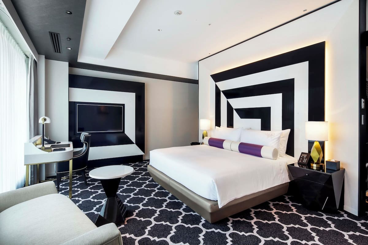 Ein modernes Hotelzimmer mit einem großen Bett, einem Schreibtisch, einem Stuhl und einem gemusterten Teppich.