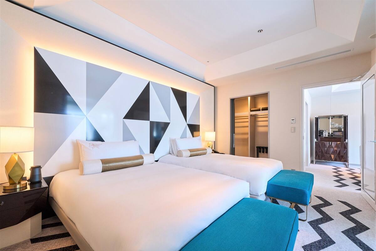 Ein Hotelzimmer mit zwei Betten, einer Minibar, einem Schreibtisch mit Lampe und einem durchgegangenen Tür erkennbaren Badezimmer.