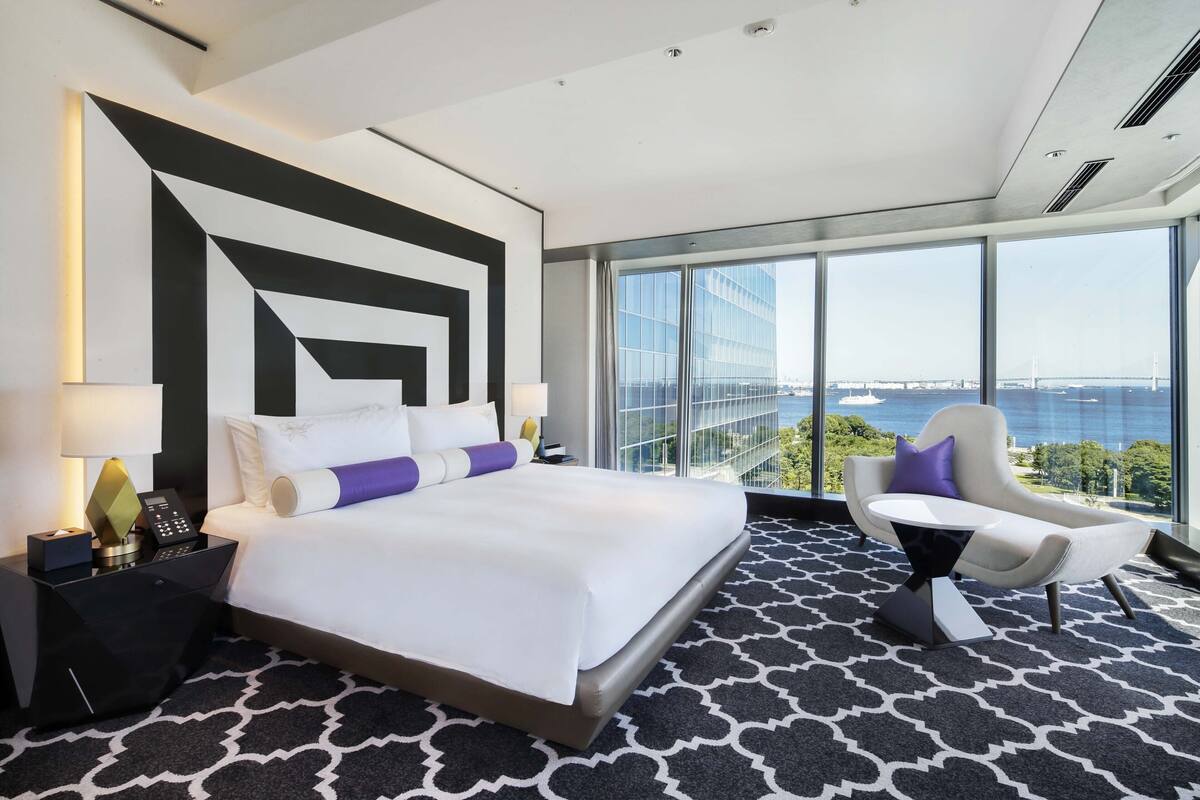 Ein modernes Hotelzimmer mit einem großen Bett, einer Sitzecke mit Blick auf die Stadt und einem großen Fenster zum Stadtbild.