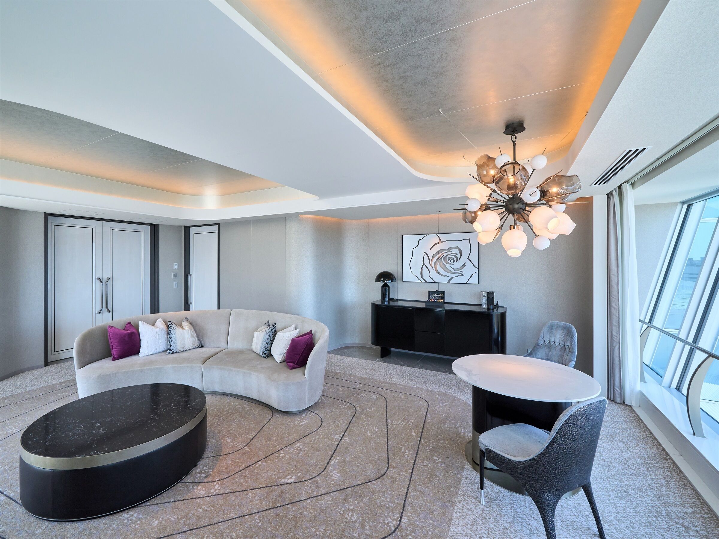 Una sala de estar moderna con un sofá curvo, una mesa redonda, una mesita auxiliar y una zona de comedor con una silla y una mesa.