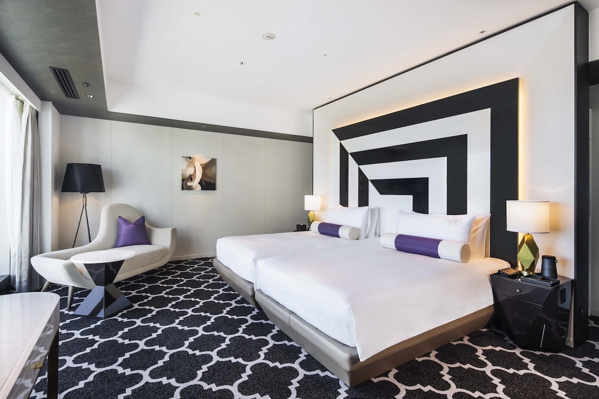 Ein Hotelzimmer mit einem großen Bett, zwei Nachttischen, einem Schreibtisch, einem Stuhl und einem gemusterten Teppich.