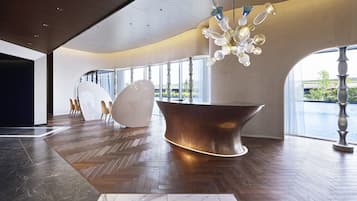 Um hall amplo com piso de madeira em padrão herringbone, uma grande bacia de cobre e um lustre moderno.