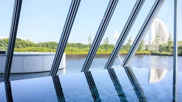 Piscina interior moderna con techo de vidrio que refleja el cielo y la vegetación circundante.