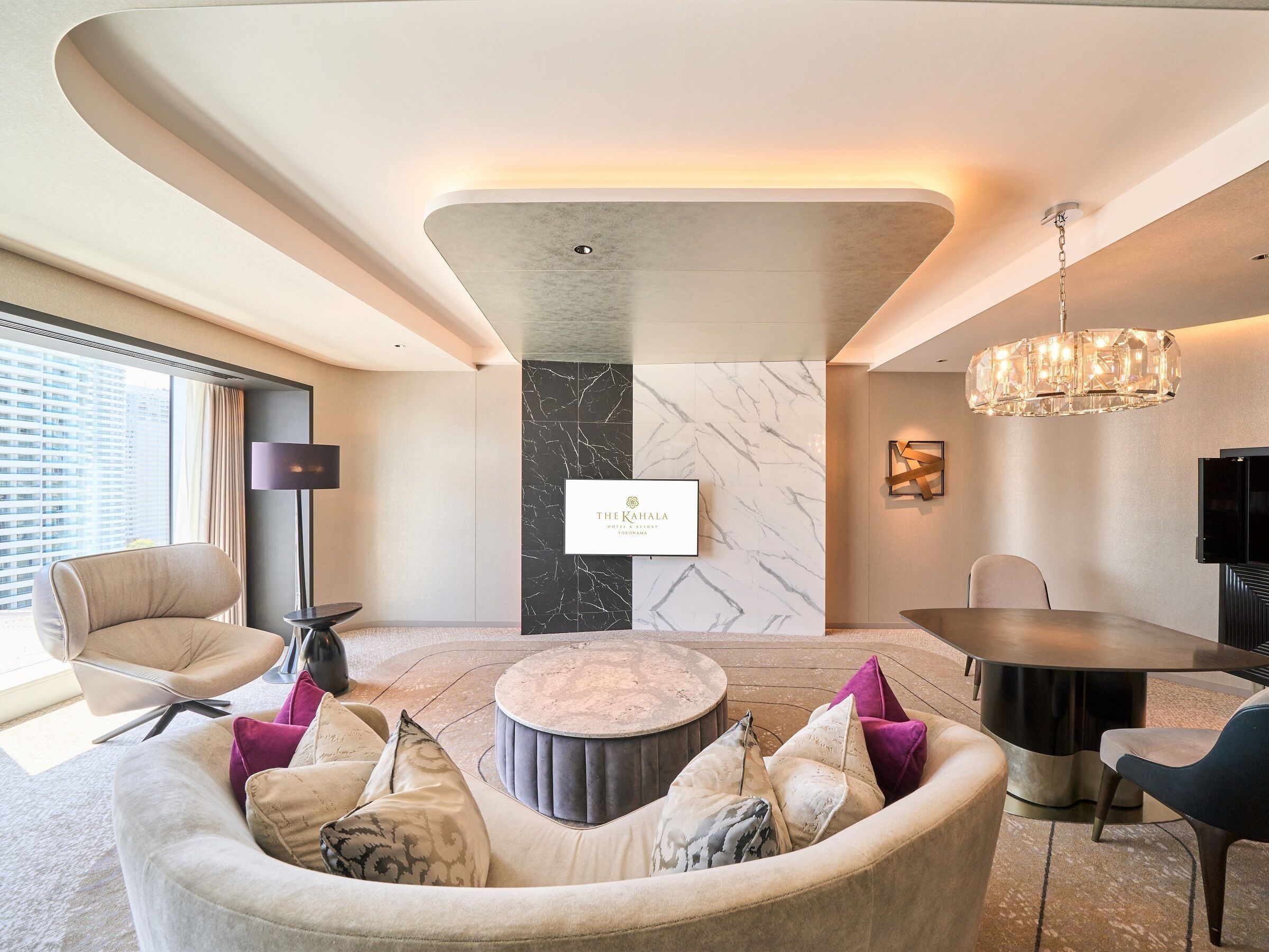 A modern hotel lobby with a curved seating area, a marble accent wall, a dining table, and a chandelier.