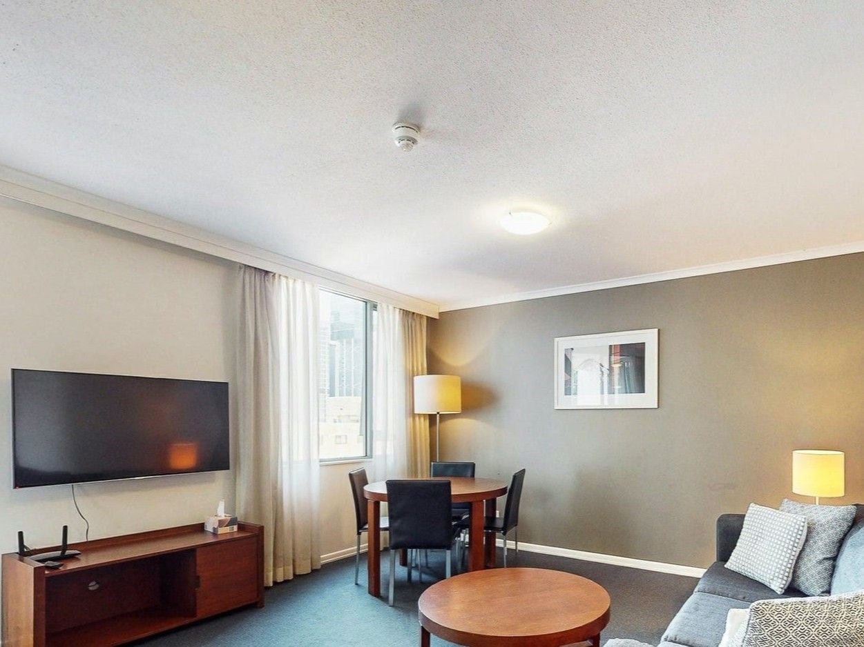Habitación de hotel con televisión de pantalla plana, una mesa de comedor con sillas, un sofá y una lámpara.