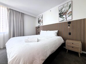 A hotel room with a large bed, a wooden headboard, a nightstand, and a wall-mounted lamp. - S&P Apartments - Albert St (Brisbane)