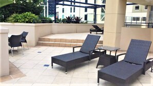 Eine Dachterrasse mit Liegestühlen und einem kleinen Tisch, umgeben von einer niedrigen Mauer und Pflanzgefäßen.