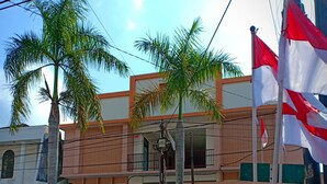 A building with a gated entrance, palm trees, and flags. - K15 Exclusive (Malang)