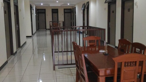 A hotel lobby with a long reception desk, multiple doors, and a tiled floor. - K15 Exclusive (Malang)
