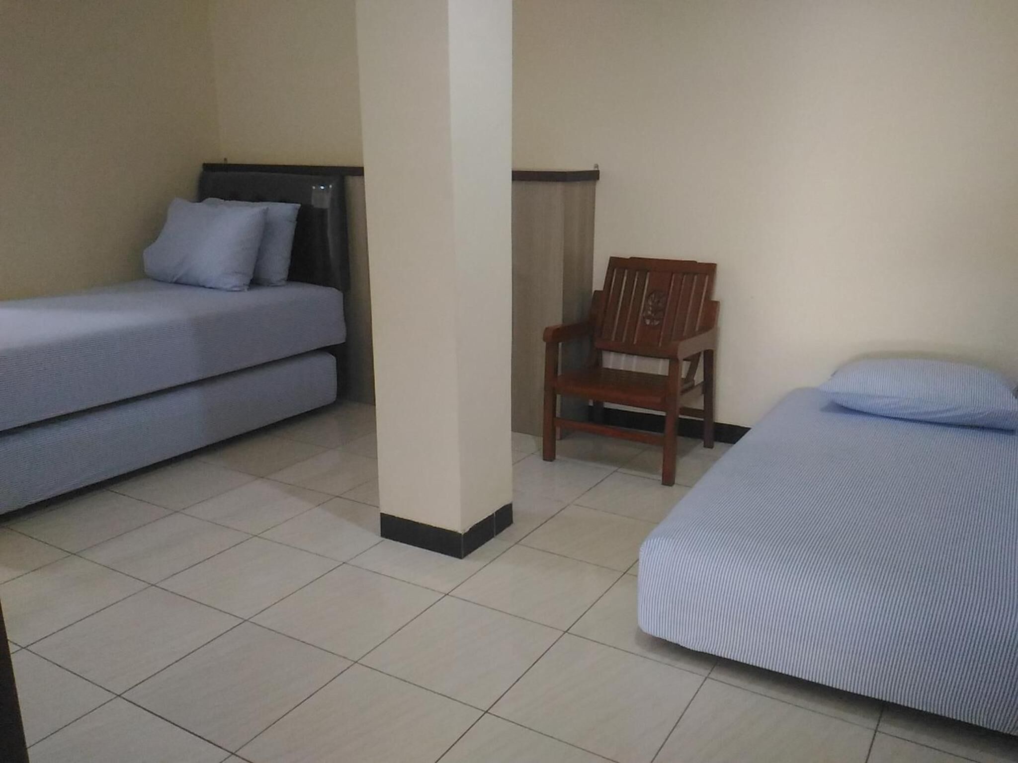 A room with two beds, a wooden chair, and a tiled floor.