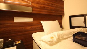 Habitación de hotel con cabecera de madera, cama con ropa blanca, mesita de noche con lámpara y espejo en la pared.