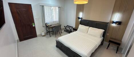 Una habitación de hotel con cama, escritorio, silla, lámpara y ventana con cortinas.