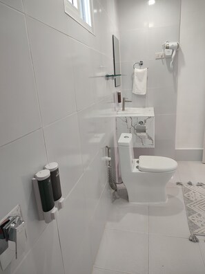 Ein modernes Badezimmer mit weißen Fliesen, einer Toilette, einem Waschbecken, einer Glasablage, einem Handtuchhalter und einer Duschkabine.