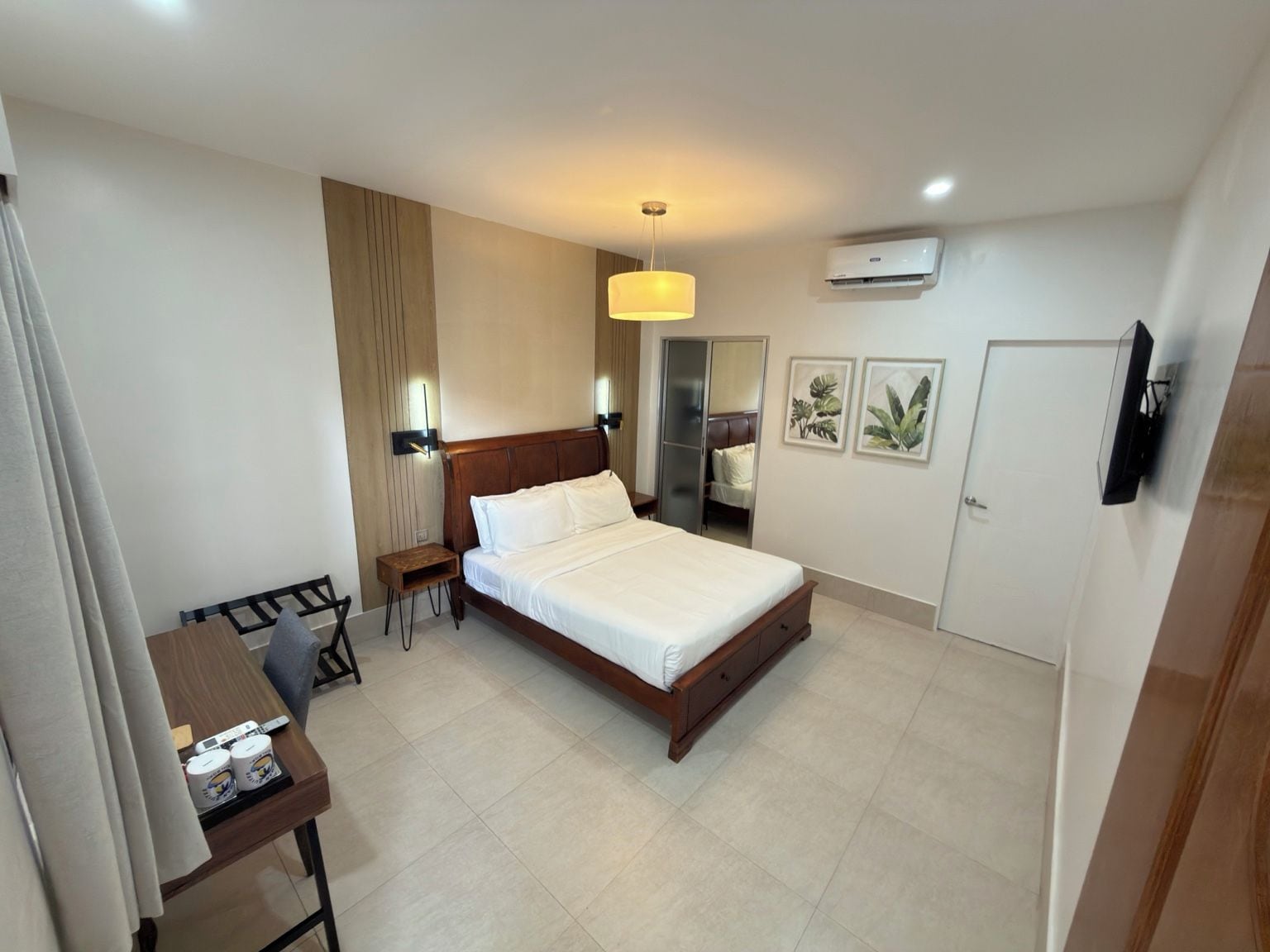 A hotel room with a bed, bedside table, chair, desk, and a television.